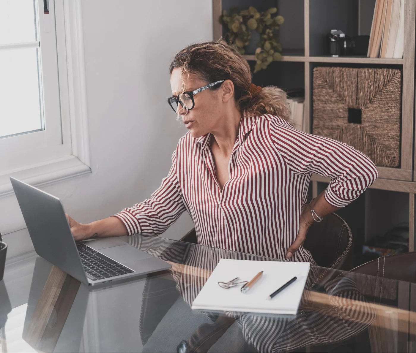 Woman working at a laptop reaching back to hold her aching lower back