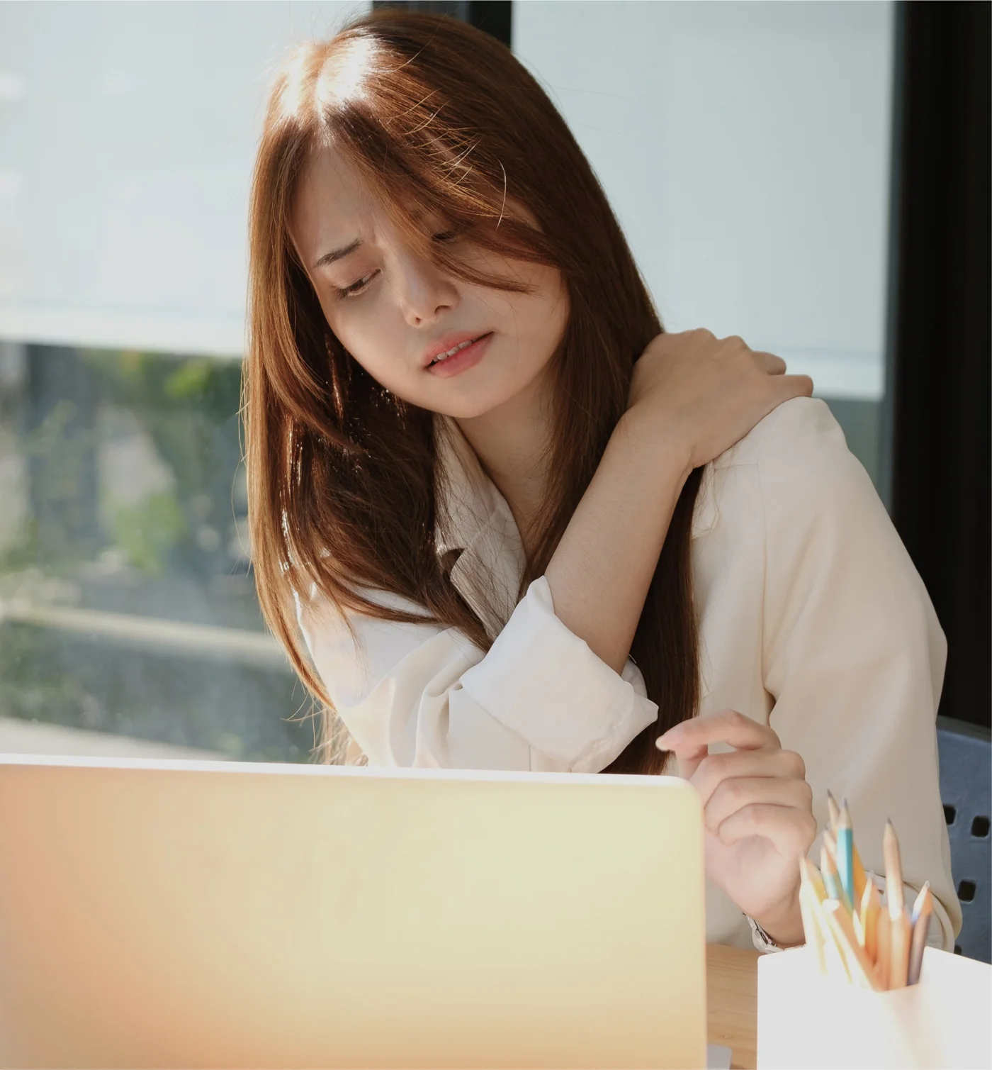 Woman at a desk pausing to hold her neck and shoulder after long hours at a laptop