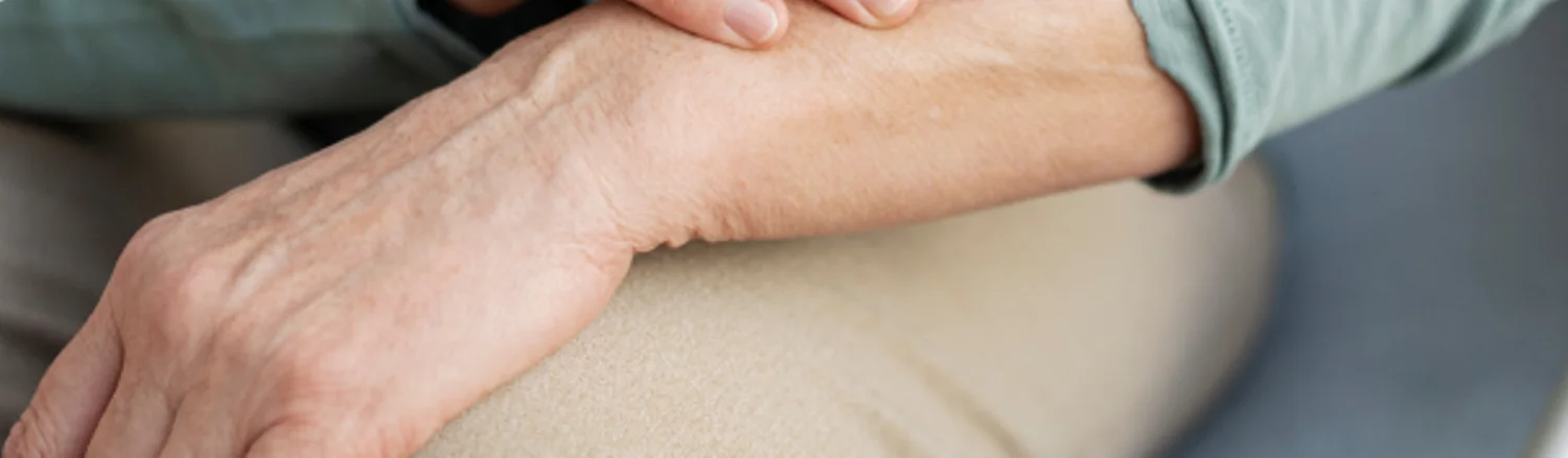Older adult’s hands resting on a knee while seated