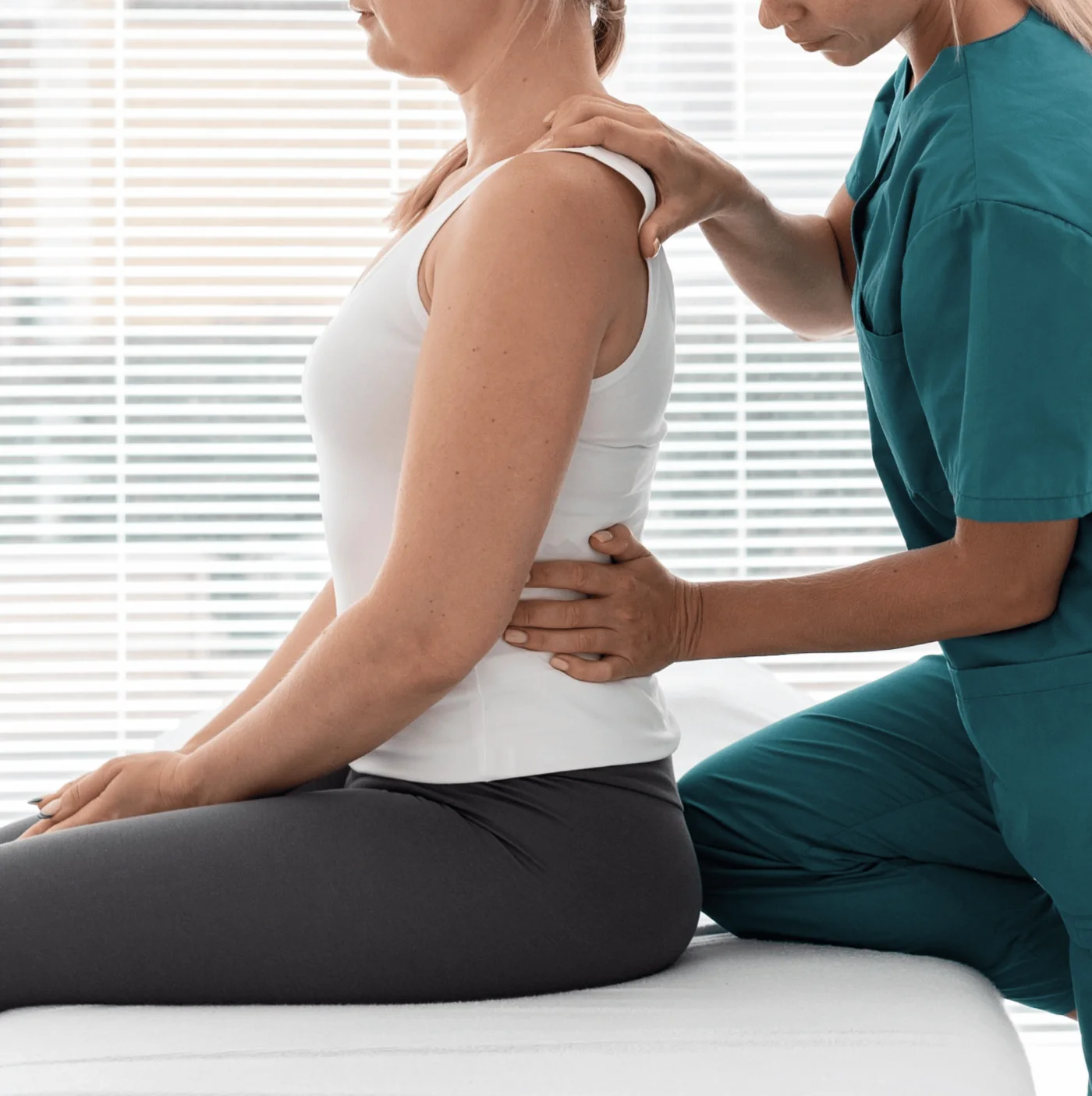 Clinician in scrubs placing both hands along the mid-back of a seated patient