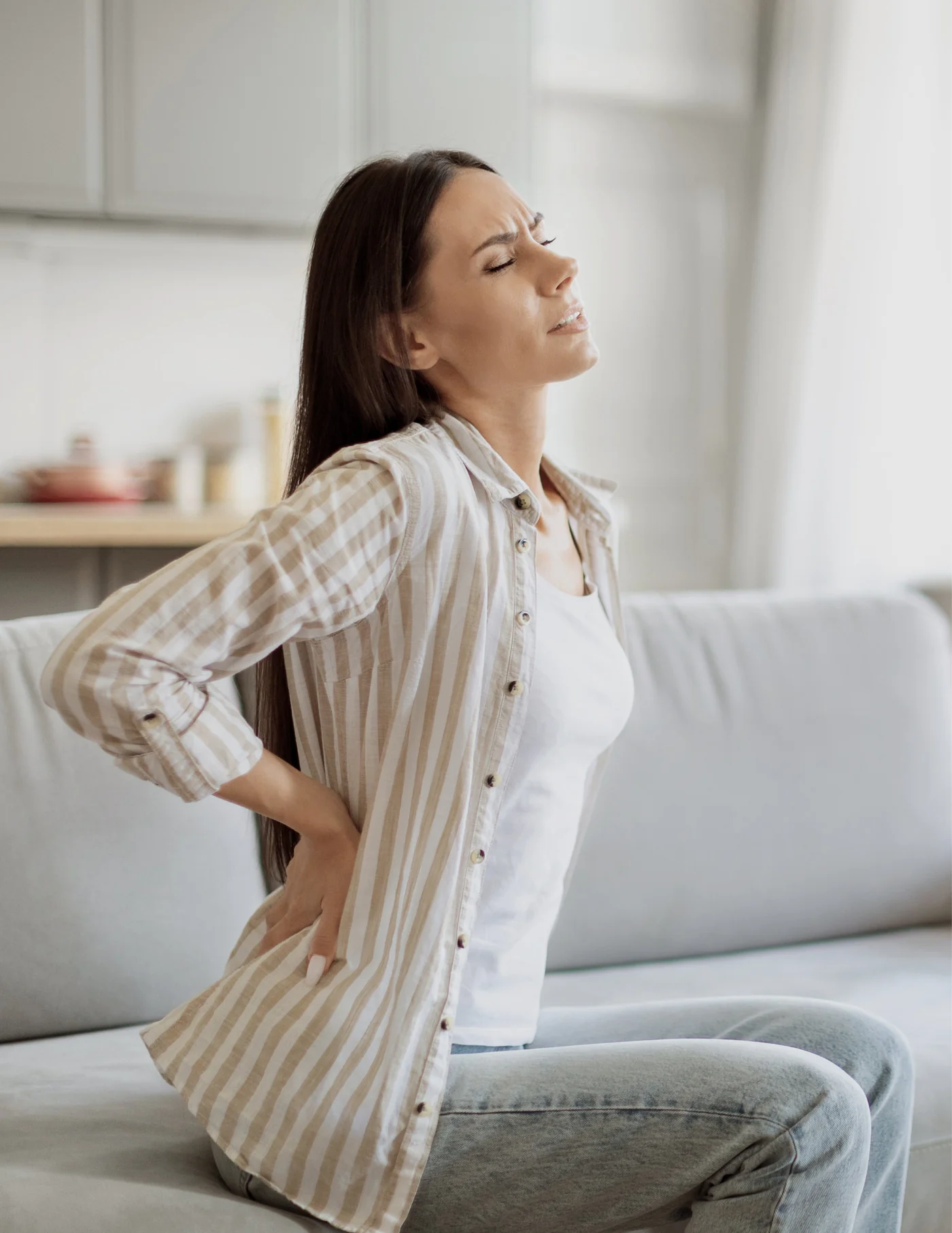Woman standing in a living room holding her lower back in discomfort