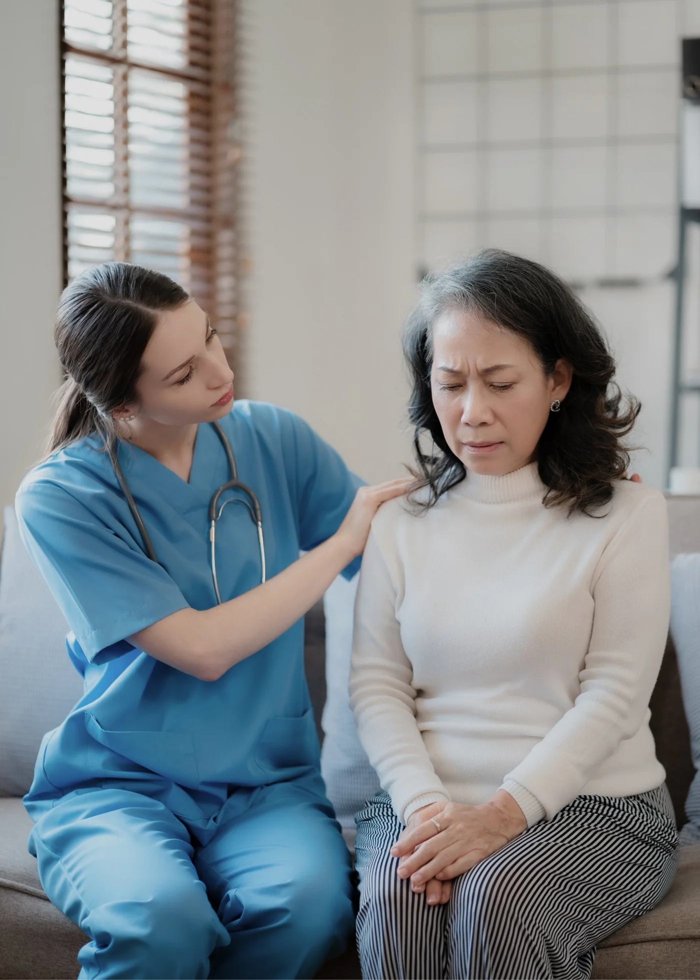 Clinician in scrubs sitting beside a patient who is holding her shoulder