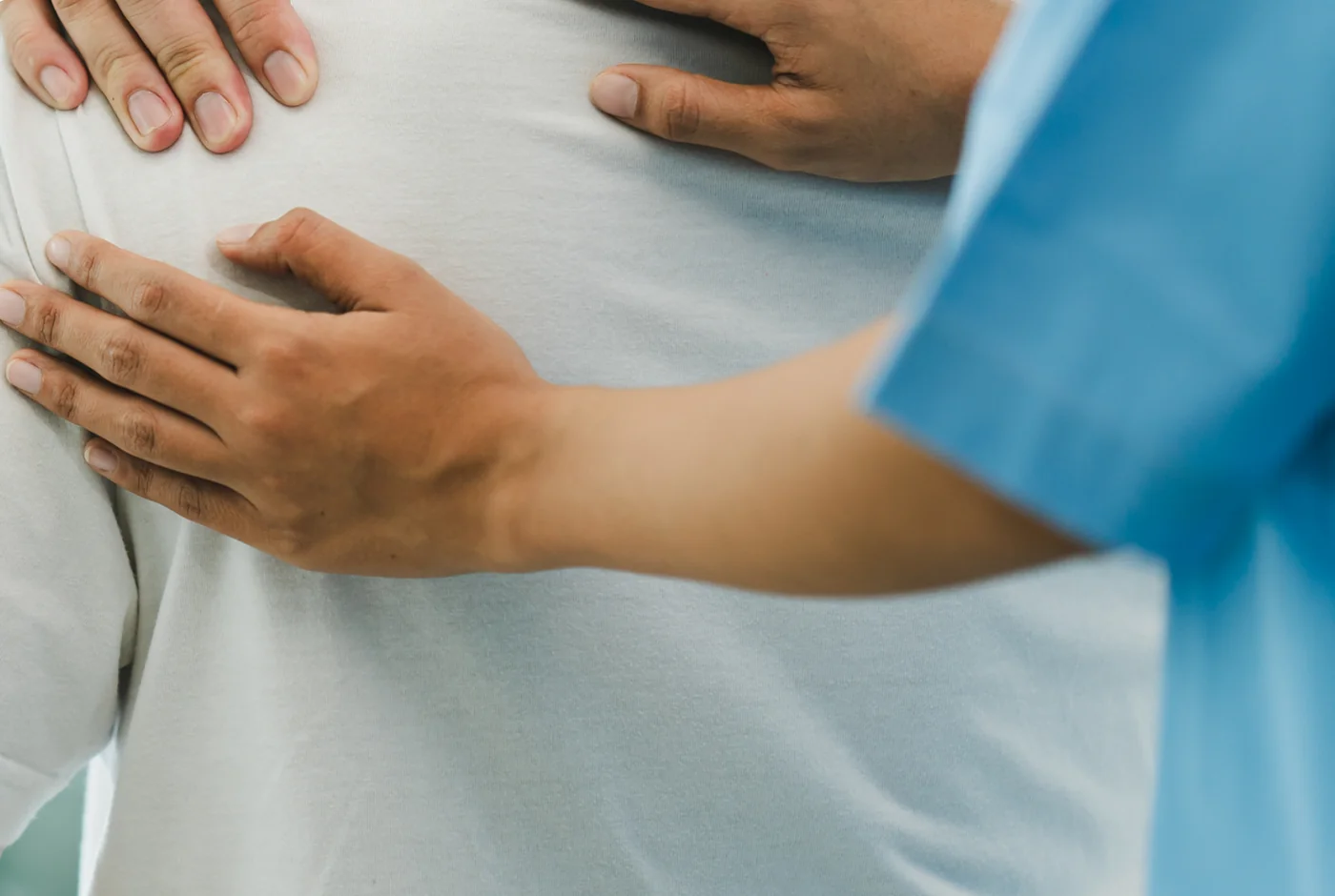 Clinician’s hands examining the shoulder blade and upper back of a patient
