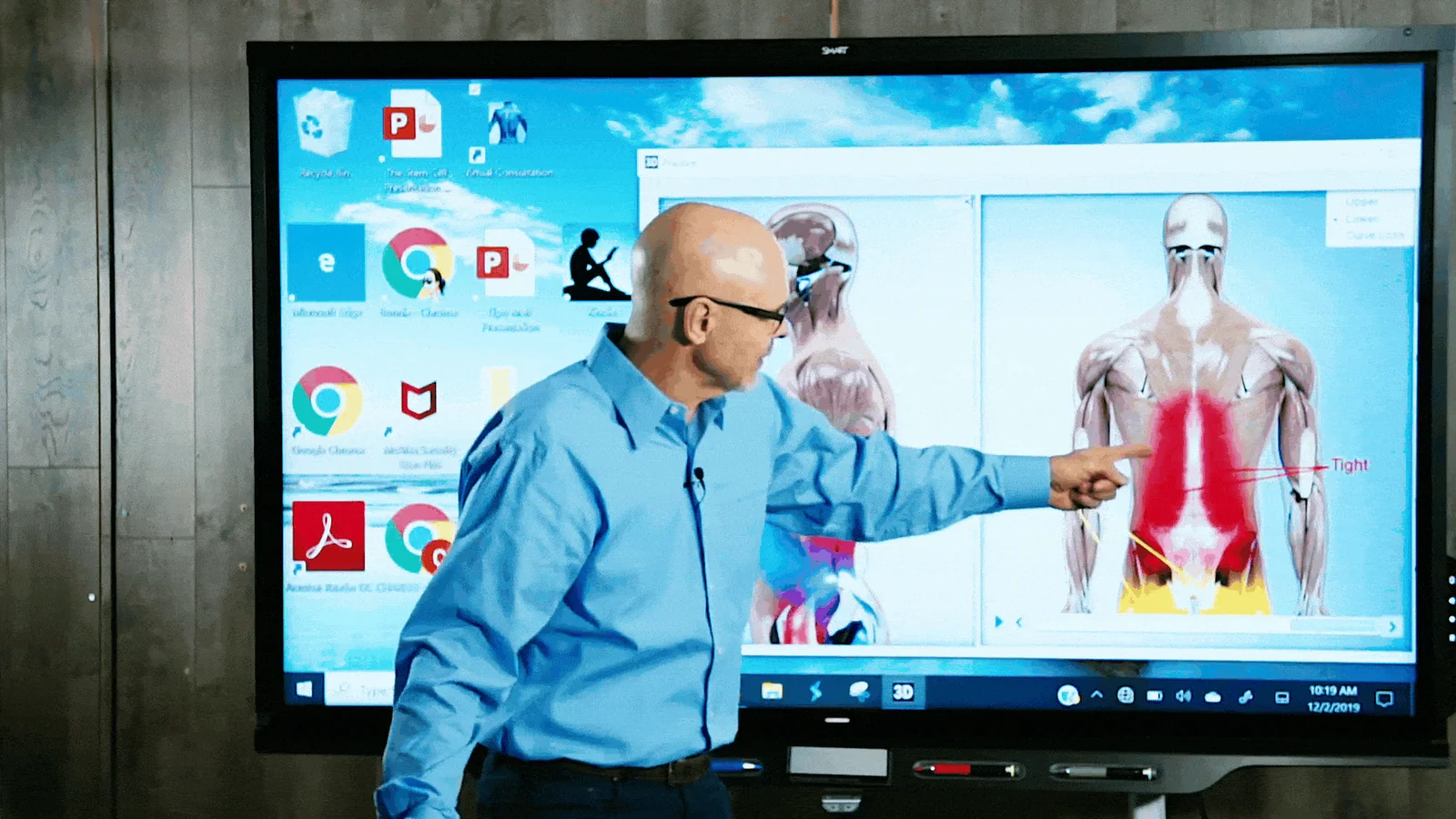 Dr. Charles Arndt pointing to a spinal anatomy image on a large wall screen during a consultation