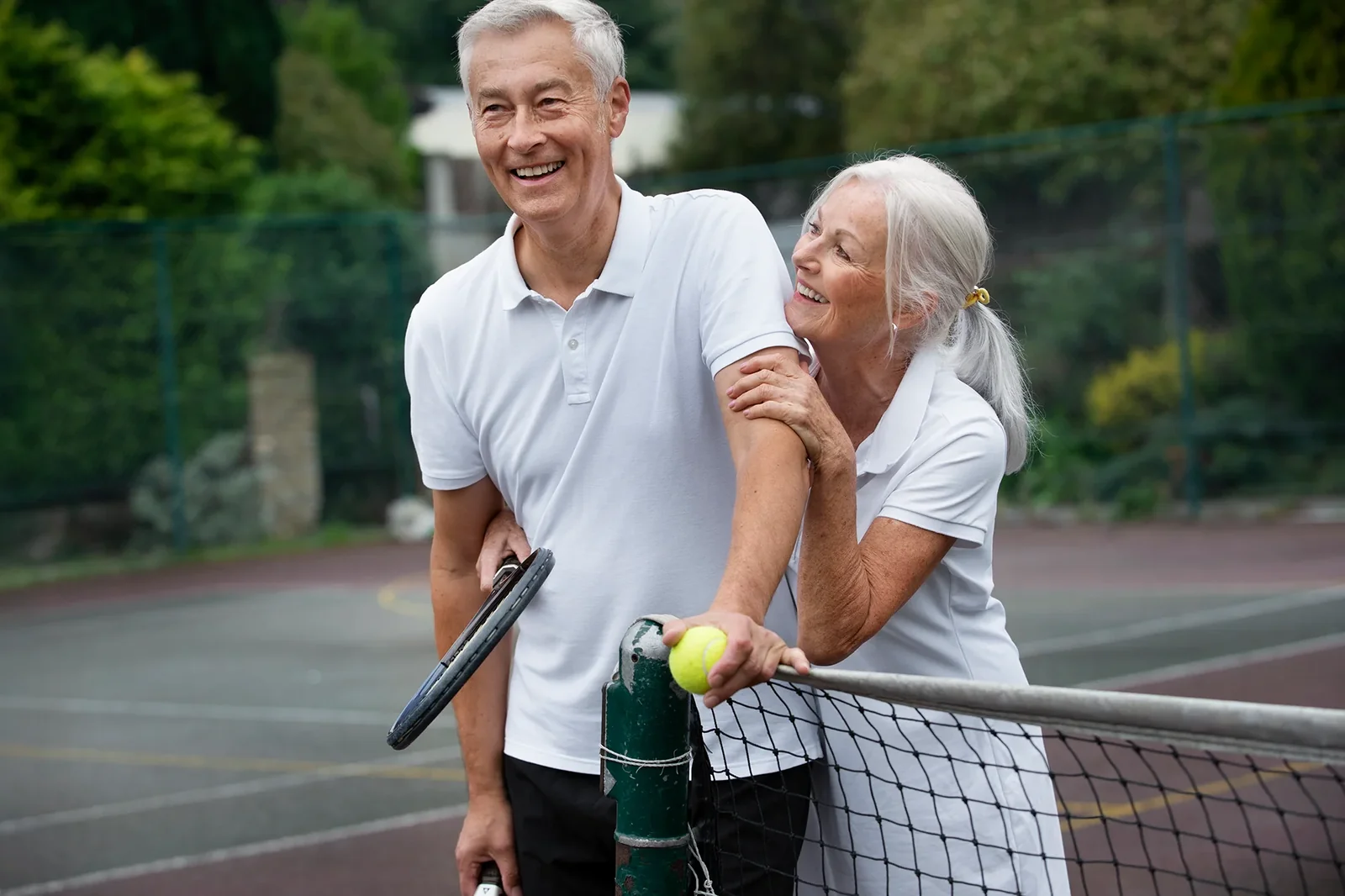 Smiling older couple standing together at a tennis net after a match