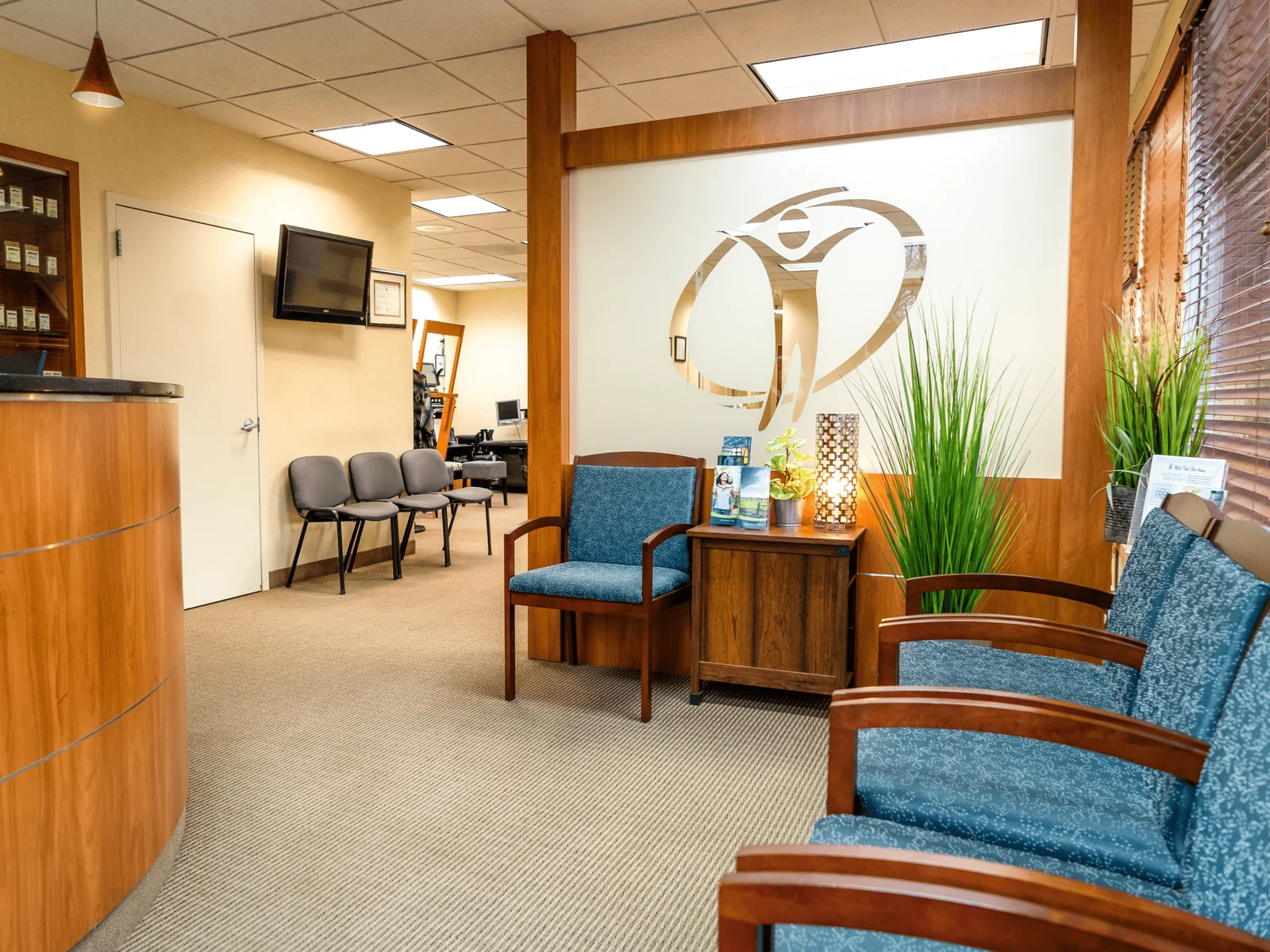 Active Lifestyle Medical reception area with wood cabinetry, teal armchairs and the clinic logo on the wall