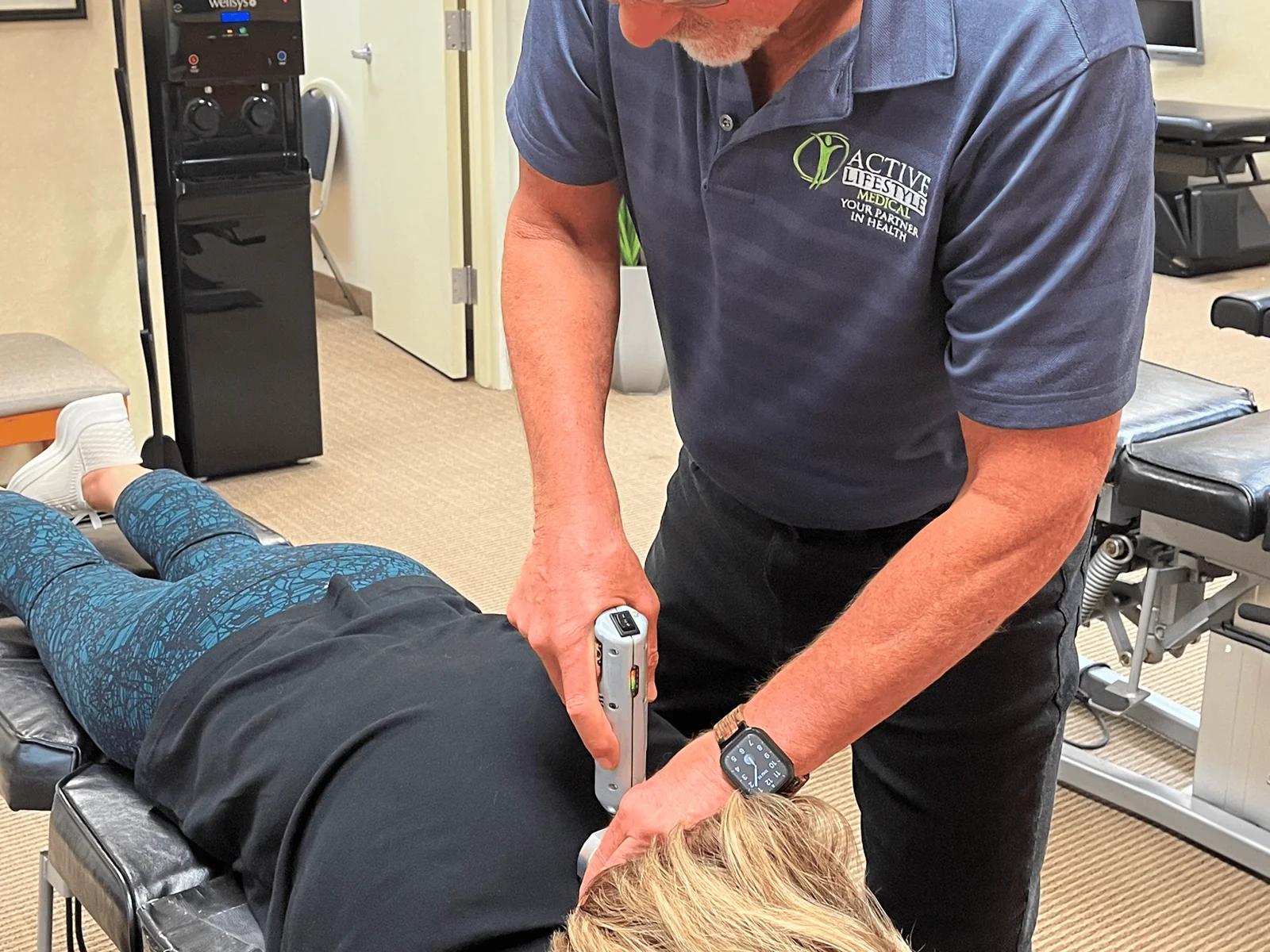 Dr. Charles Arndt using a handheld adjusting instrument along the neck of a patient lying face down on a treatment table