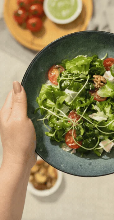 Hand lifting a bowl of fresh salad from a table set with whole foods
