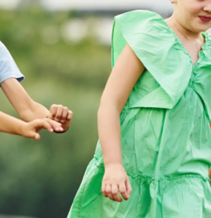 Young child in a green dress holding an adult’s hand outdoors