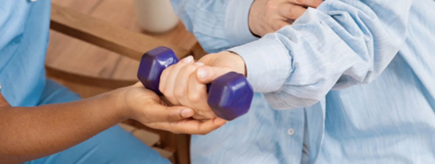 Therapist supporting an older patient’s arm through a light dumbbell exercise
